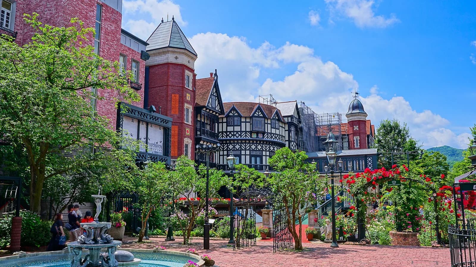 Shiroi Koibito Park's rose garden and Tudor-style buildings on a sunny day in July 2026. The garden is outdoors; one wing shows renovation scaffolding. Resized and converted to WebP.